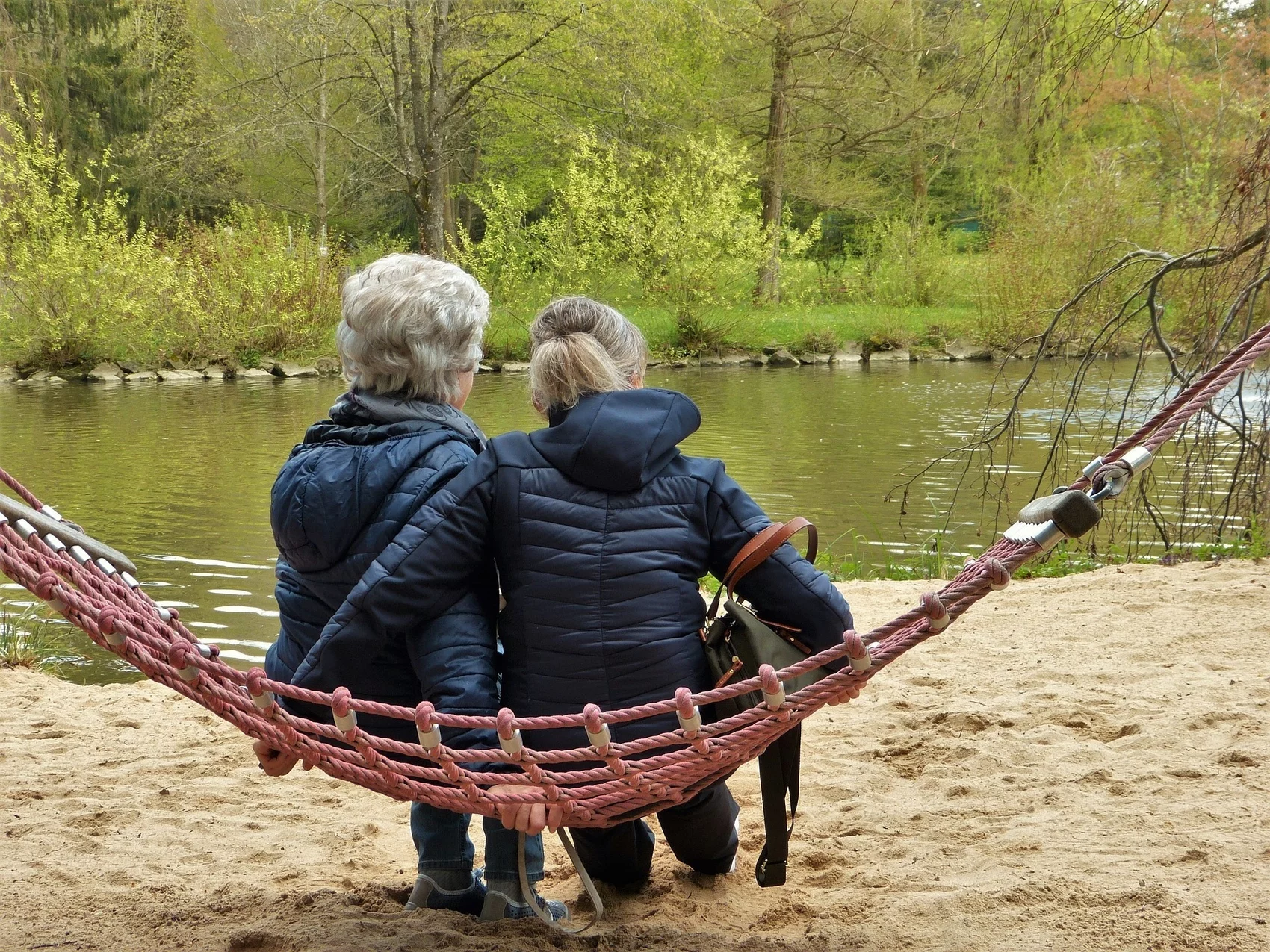 Zwei Frauen sitzen auf einer Hängematte und Blicken auf das Wasser.